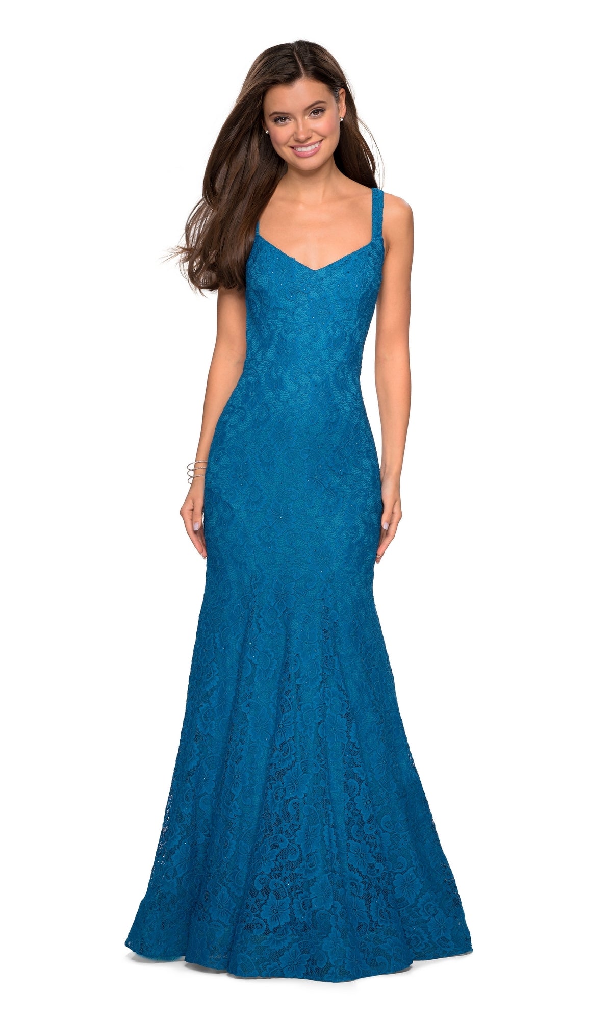 A woman stands and smiles in a sleeveless, floor-length teal blue La Femme 27709 open-back lace mermaid prom dress featuring a fitted bodice and flared skirt.